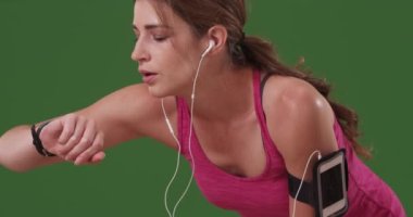 Genç milenyum kadını yeşil ekranda koşarken bileğindeki spor takip cihazını kontrol ediyor. Anahtar ya da birleşik olmak üzere yeşil ekranda.