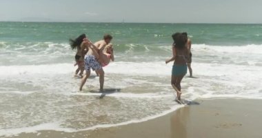 Plajda mayo giyen çok ırklı bir grup mutlu arkadaş oynuyor.