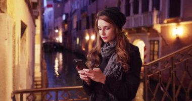 Venedik, İtalya 'da gezmeye çıkmış beyaz bir kadın. Venedik 'teki çekici esmer kadın dışarıda telefonuna blog yazısı yazıyor. 4k
