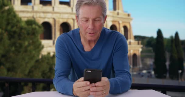 イタリアのローマを旅行している男は スマートフォンで面白いメッセージを受け取ります ローマのコロッセオ近くに座っていた白人男性はテキストに反応し 電話をかけます — ストック動画