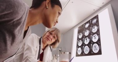 Genç bir hastayla röntgenlere bakan olgun beyaz kadın doktor.