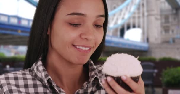 魅力的なラティーナは ロンドンで素敵な一日においしいカップケーキを食べます 幸せな笑いヒスパニック系の女の子は甘いおいしいペストリーを楽しんでいます — ストック動画