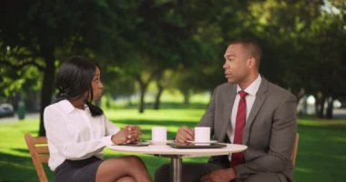 İki iş adamı açık kafede mi buluşuyor? Park yerinde. Siyah iş adamı ve kadın tablet bilgisayar kullanıyor ve birlikte kahve içiyorlar..