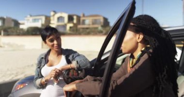 Kız arkadaşlar plajda arabaya yaslanıp konuşuyorlar ve telefonla mesajlaşıyorlar.