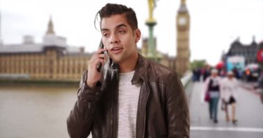 Havalı ve yakışıklı İspanyol erkek Big Ben 'in yanında telefonda konuşuyor. Deri ceketli bin yıllık bir adamın Londra 'da cep telefonuyla sohbet edişinin portresi. 4k