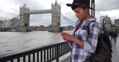 Millennial etnik güzellik Londra, İngiltere 'yi gezerken telefonunu kontrol ediyor. Londra 'daki siyahi kadın turist Tower Köprüsü yakınlarında bir mesaj gönderiyor. 4k