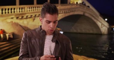 Yakışıklı ve modaya uygun Latin erkek Venedik 'te gece telefonuna cevap veriyor. Rialto Köprüsü 'nde cep telefonuyla konuşan mutlu milenyum çocuğunun portresi. 4k