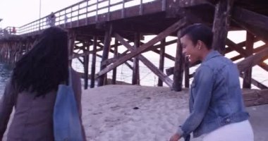 Gün batımında iskelede yürüyen iki mutlu siyah kadın.