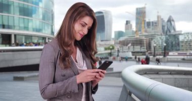 Kendine güvenen genç iş kadını şehir merkezinde telefonunu kontrol ediyor. Genç beyaz kadın profesyonel Londra 'da akıllı telefonunu kullanıyor. 4k