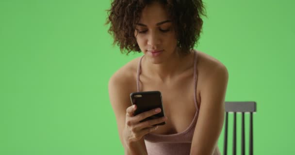 一个年轻的非洲裔美国女孩 卷发短发 用她的智能手机在绿色屏幕上看书 在绿色屏幕上键入或合成 — 图库视频影像