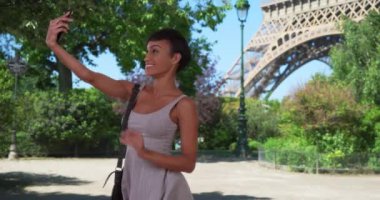 Paris 'teki Eyfel Kulesi yakınlarında akıllı telefonuyla selfie çeken neşeli, genç, melez bir kadın. Fransa 'da seyahat eden eğlenceli bir milenyum kadını kendi fotoğrafını çekiyor. 4k