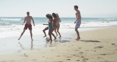 Sahilde top oynayan eğlenceli çoklu etnik arkadaş grubu.