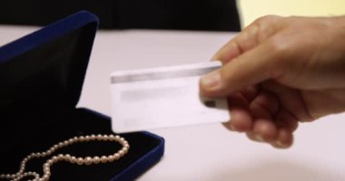Yetişkin bir beyaz erkeğin mücevher satın almasına yakın çekim. Kolyenin parasını kredi kartıyla ödeyen kıdemli adam..