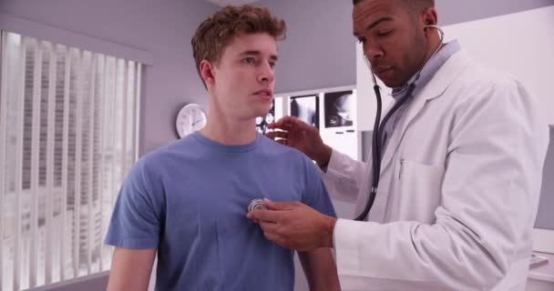 아프리카 미국인 의사가 청진기를 사용하여 코카서스 환자의 듣는다 — 비디오