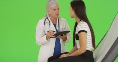 Yaşlı bir doktor yeşil ekranda tabletini kullanırken check-up yaptırıyor. Anahtar ya da birleşik olmak üzere yeşil ekranda.