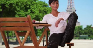 Paris, Fransa 'da Eyfel Kulesi' nin yanındaki sandalyede poz veren çarpıcı bir zenci kadın manken. Güzel Afro-Amerikalı kadın Eyfel Kulesi 'nin önünde kameraya dik dik bakıyor. 4k