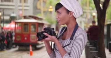 Kameralı bir kadın arka planda tramvayla San Francisco caddesinde fotoğraf çekiyor. Yirmili yaşlardaki turist kız tatile çıkıyor.