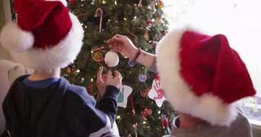Genç beyaz çocuk babama Noel ağacı süslemesinde yardım ediyor.