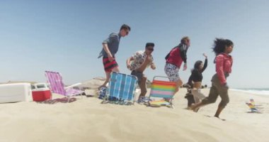 Sahilde ağır çekimde koşan ırklar arası genç bir grup.