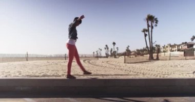 Siyahi kadın sahildeki kısa duvarda dengede durup gülümsüyor.