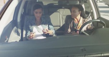 İki siyahi kadın arkadaş arabada oturmuş birbirleriyle konuşuyor ve gülümsüyorlar.