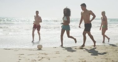 Sahilde top oynayan çok ırklı, sağlıklı bir grup genç arkadaş.