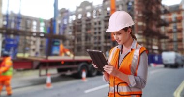 Çalışkan Kafkasyalı kadın inşaat işçisi ped cihazının planlarını inceliyor. Şehirde inşaat alanında çalışan genç beyaz bir kadın. 4k