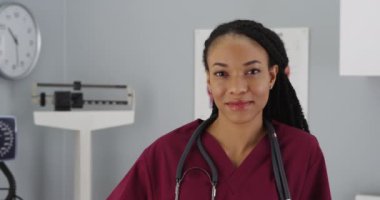 Genç siyah kadın doktor kameraya gülümsüyor.