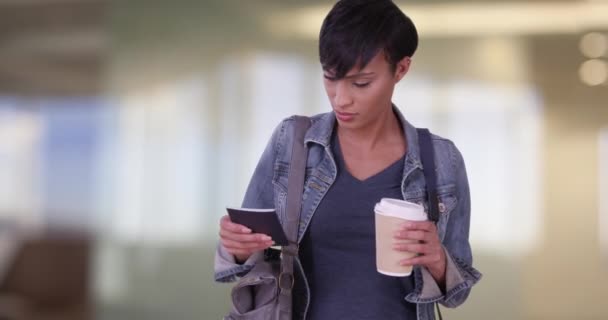 空港でコーヒーを持ちながらフライトを待っている間 大きな財布の中にパスポートを探している黒人女性 ミレニアルで彼女の20代のフライトを待っているジャンジャケットを着て — ストック動画