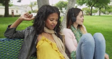 Mutlu kız arkadaşlar bankta müzik dinliyor.