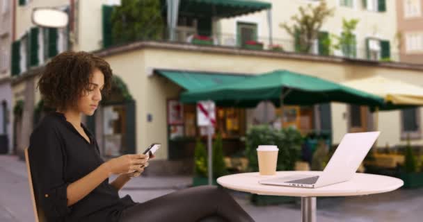 在户外咖啡馆使用智能手机装置的普通黑人妇女 坐在餐厅外面看手机手持式技术的女性画像 — 图库视频影像