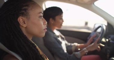 İki siyahi kadın arkadaş arabada oturmuş birbirleriyle konuşuyor ve gülümsüyorlar.