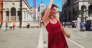 İtalya, Venedik 'teki St. Mark Meydanı' nda neşeyle dans eden genç, seksi, beyaz esmer. İtalya 'da tatilde dans eden kırmızı elbiseli mutlu genç bir bayan. 4k