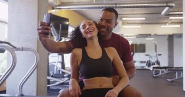 Spor salonunda gülümseyen ve selfie çeken tatlı siyah ve İspanyol çift.