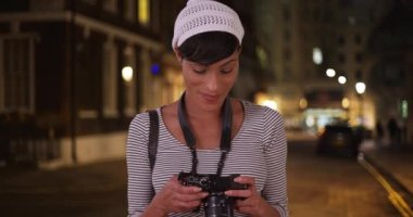 Kaliteli etnik fotoğrafçı, şehirde bir fotoğraf çekimindeyken çektiği bazı fotoğraflara bakıyor. Kadın siyahi kadın gece şehir ortamında fotoğraf çekiyor. 4k