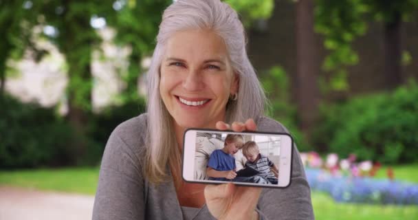 Bahçede Oturan Yaşlı Beyaz Bir Büyükanne Genç Torunlarının Videosunu Göstermiş — Stok video
