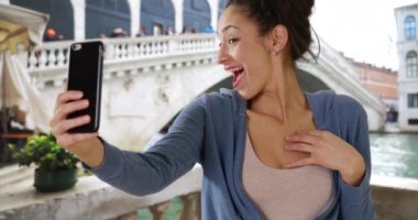 Şirin gülümseyen Latin kadın Grand Canal yakınlarında selfie çekiyor. İtalya 'yı gezen genç ve çekici bir kadın cep telefonuyla kendi fotoğrafını çekiyor. 4k