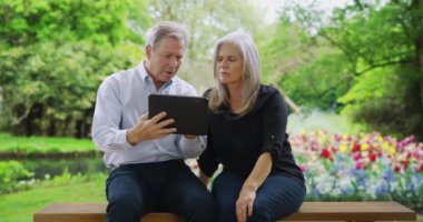 Parktaki bankta oturan yaşlı çift tabletlerini kullanarak nerede olduklarını anlamaya çalışıyor. Üst düzey beyaz adam ve kadın internet üzerinden adres araştırması yapıyorlar. 4k