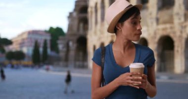 Roma, İtalya 'da tatil yapan umursamaz bir kadın Colosseum' un önünde kahveli hamur işi yiyor. Roma Kolezyumu 'nun önünde gelişigüzel dikilen çekici Afrikalı kadın. 4k