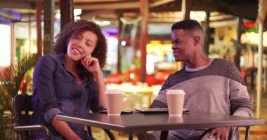 Milenyum siyahi çifti kafede kahve mi içiyor? Geceleyin. Genç Afro-Amerikalı erkek ve kadın tabletlerini ve akıllı telefonlarını kullanırken içki içiyorlar. 4k.