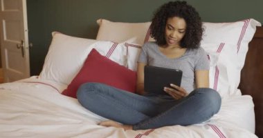 Siyah kadın evde tablet kullanarak yatakta oturuyor.