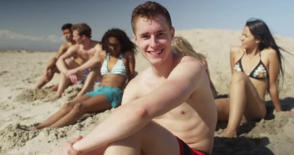 Plaj Gülümseyen Arkadaşlar Ile Kuma Oturan Genç Beyaz Adam Portresi — Stok video