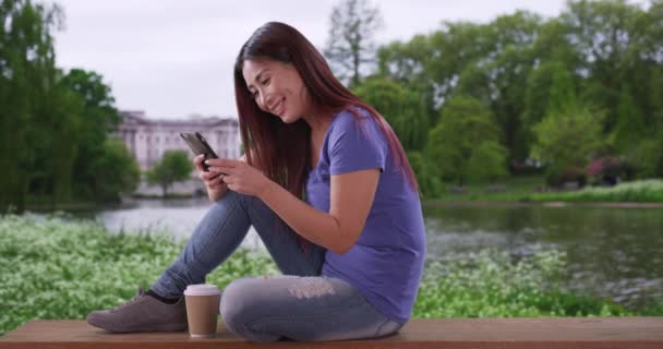 快乐的日本女性在圣詹姆士公园发短信给她的男朋友 在公园里微笑着喝着咖啡和发短信的迷人女人 — 图库视频影像