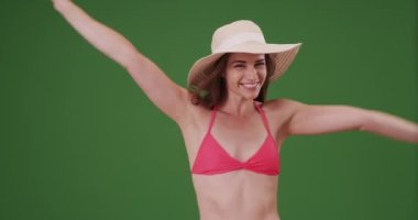 Yeşil ekranda şapka ve bikini giyerken kamerayla flört eden seksi kadın. Anahtar ya da birleşik olmak üzere yeşil ekranda.