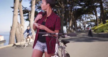Bisikletli bir kadın San Francisco 'daki parktaki akıllı telefondan mesaj yazma uygulaması kullanıyor. Mutlu, çekici, 20 'li yaşlarda siyah bir kadın.