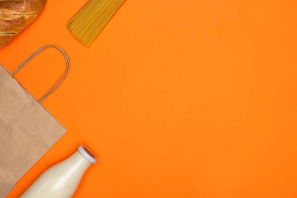 Паперовий еко-пакет, скляна пляшка молока, хліба та спагеті на яскраво-оранжевому ізольованому фоні — стокове фото
