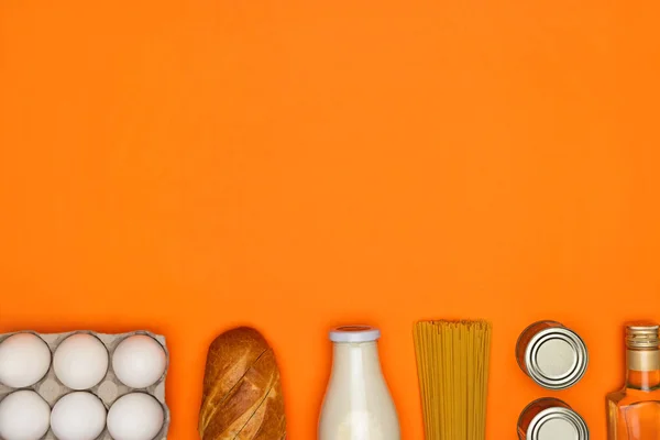 Скляна пляшка молока, білі яйця, спагеті, оливкова олія, хліб, металева олова на яскраво-помаранчевому фоні — стокове фото