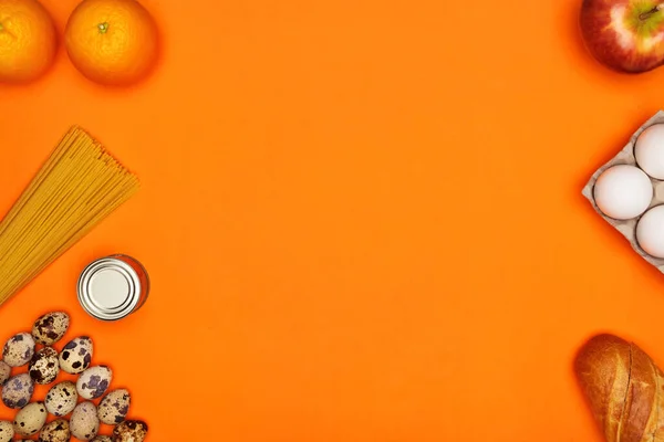 Білі та перепелині яйця, спагетті, хліб, апельсини, червоне яблуко, металева олова на помаранчевому фоні — стокове фото