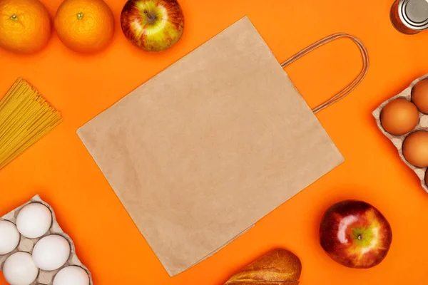 Паперова еко сумка, яйця, спагетті, хліб, червоні яблука, апельсини та металева олова на яскраво-оранжевому ізольованому фоні — стокове фото