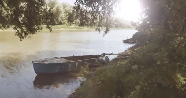 Старая голубая лодка, привязанная веревкой к деревянному пирсу, плавно скачет по течению реки. — стоковое видео